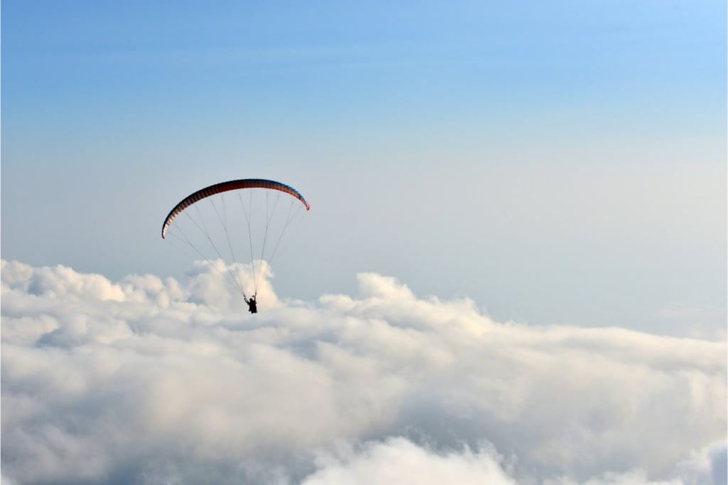 A paraglider pilot soars over the clouds