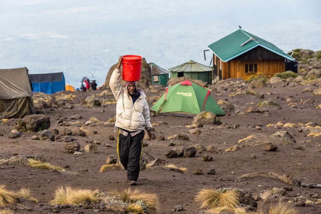 Портер несет емкость с водой в лагере на Килиманджаро